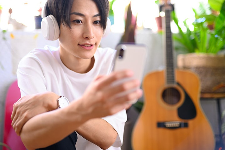 ギタトレ@マスターで100講座以上のオンラインギターレッスンをスマホで受講する男性
